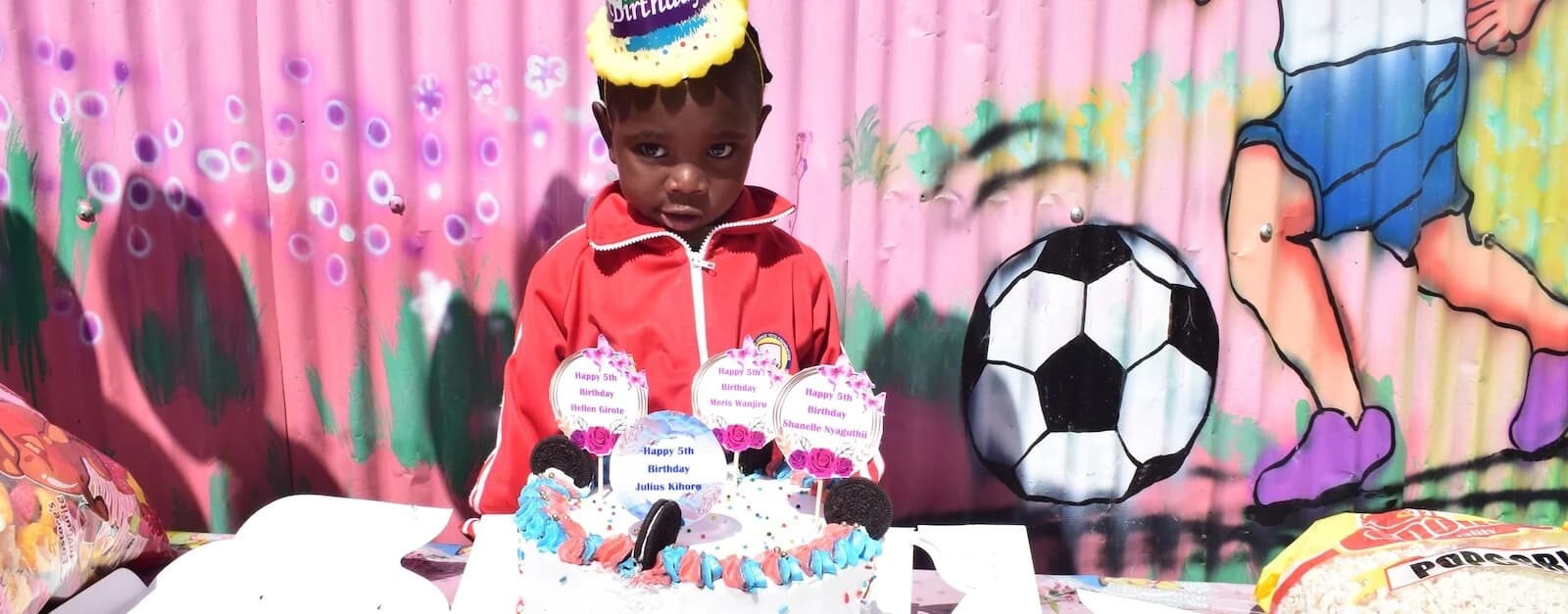 A child standing behind a birthday cake during an orphan care celebration