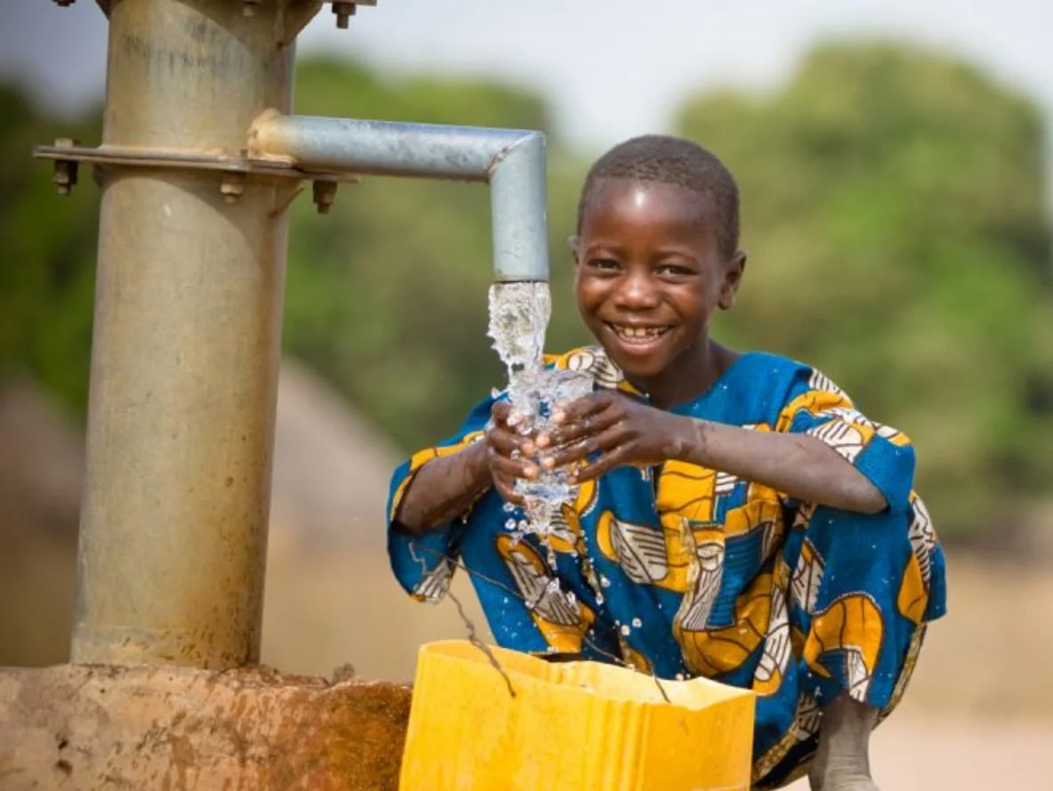 Child drinking water from a tap, illustrating the impact of water well projects